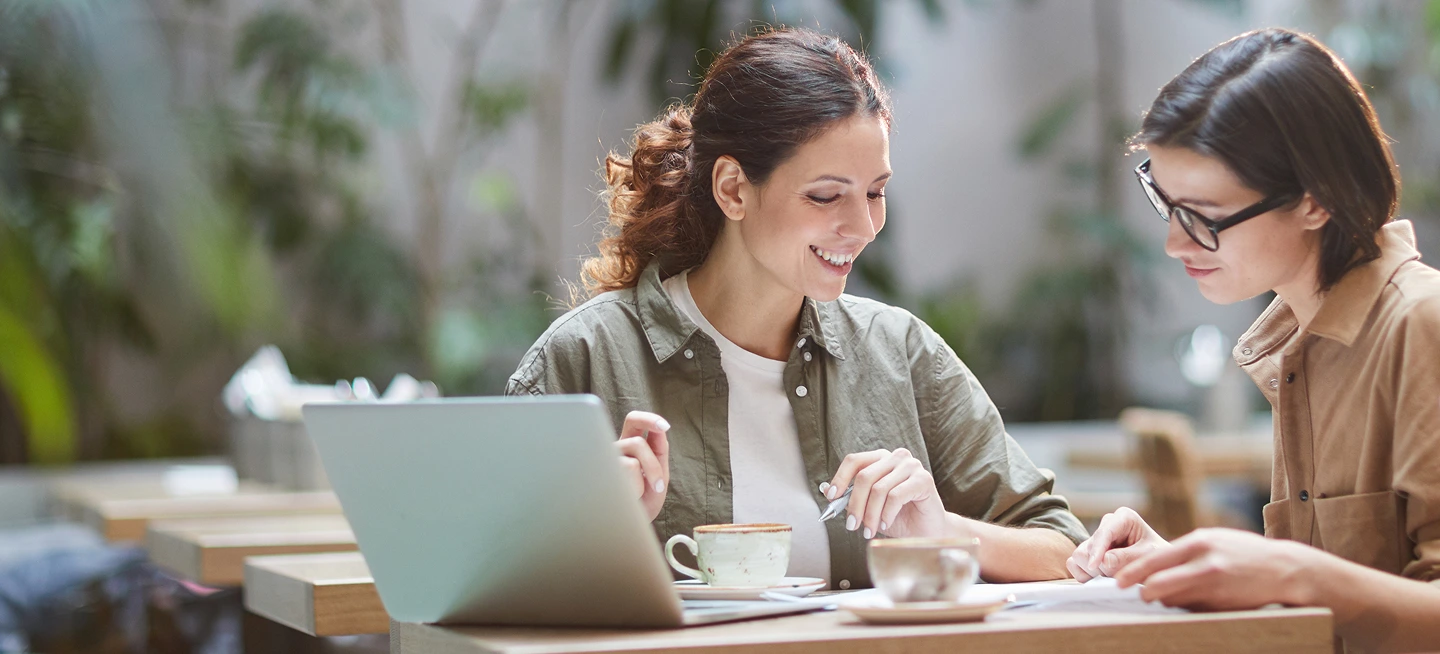 Deux femmes souriantes coworkant ensemble autour d'un ordinateur portable.